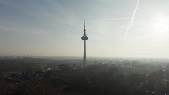 Aerial footage slowly approaching Fernmeldeturm Mannheim, telecommunication tower surrounded by a hazy and foggy cityscape