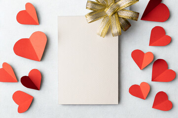 Blank card surrounded by red paper hearts and a golden ribbon
