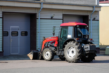 A tractor with a red roof is parked beside a building featuring a gray exterior and large windows...