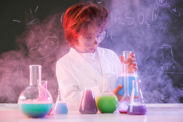 Back to school. Boy doing chemical research at desk against chalkboard with formulas indoors