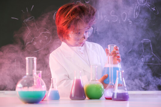 Back to school. Boy doing chemical research at desk against chalkboard with formulas indoors