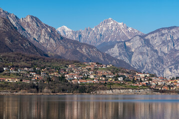 Serene landscape featuring a tranquil lake with a small town nestled on a hillside, beneath majestic, snow-capped mountains