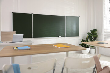 Green chalkboard, backpacks and stylish furniture in classroom. Mockup for design