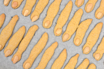 An overhead shot of numerous freshly baked sugar cookies shaped like spooky witch fingers with almond fingernails, laid out on a baking sheet
