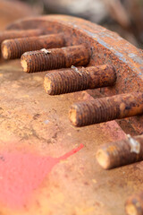 Close-up view of a row of heavily rusted metal studs and bolts on a machine flange, showing severe corrosion and degradation on the surface.