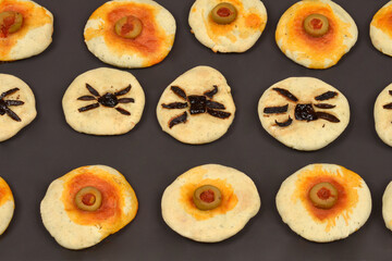 An overhead shot of freshly baked Halloween appetizers, featuring mini pizzas decorated with olives and dark toppings to resemble eyeballs and spiders on a baking tray