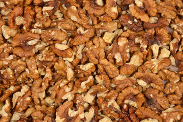 A full frame close-up shot of a densely packed, unorganized pile of shelled walnut halves and pieces, showcasing their texture and color variation