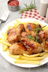 Grilled chicken drumsticks served with french fries and spices on grey table, closeup