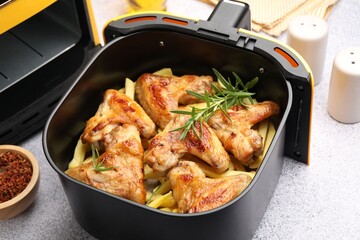 Grilled chicken wings with french fries in air fryer basket and spices on grey table, closeup