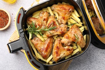 Grilled chicken wings with french fries in air fryer basket and spices on grey table, flat lay