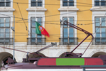 lisboa, tranvia electrico en la plaza del comercio con la bandera de portugal.