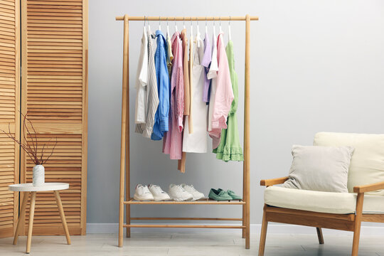 Different stylish clothes hanging on rack, shoes and armchair near light wall indoors