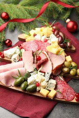 Delicious Christmas Charcuterie board with snacks, fir branches and baubles on grey textured table
