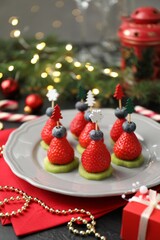 Christmas food. Tasty canapes with strawberries, kiwi, blueberries and decor on black table, closeup. Bokeh effect