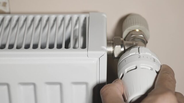 Save energy: close up of Hand Adjusting Heating Thermostat, one hand operates the temperature controller radiator,