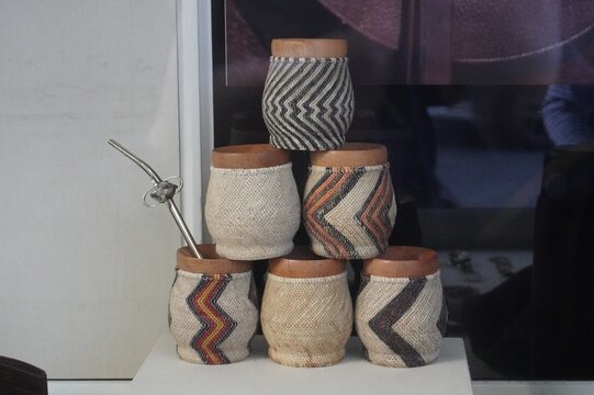 Stack of handcrafted mate gourds covered with woven fabric patterns, displayed with a metal straw. Traditional South American design highlighting artisanal craftsmanship and cultural heritage.