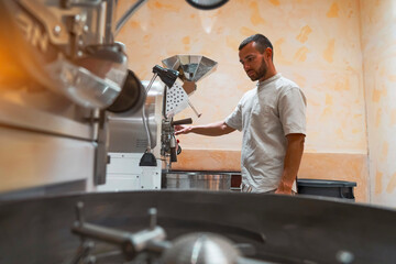 Worker carefully operates a coffee roasting machine, preparing arabica and robusta beans in a workshop. The setup is efficient and designed for optimal roasting, showcasing craftsmanship