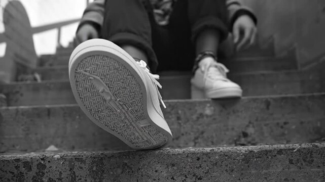 A dynamic low-angle perspective captures a person's foot in a clean, white sneaker making contact with a textured concrete stair. The detailed tread and pattern of the shoe's sole are clearly visible 