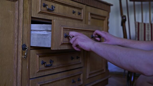 Hands carefully put away a green cloth into a vintage wooden dresser drawer, showcasing daily domestic organization and storage in a home interior.