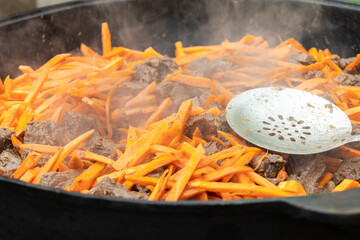 Sizzling beef and carrot stir-fry cooking in a large pan at a bustling outdoor market during a...