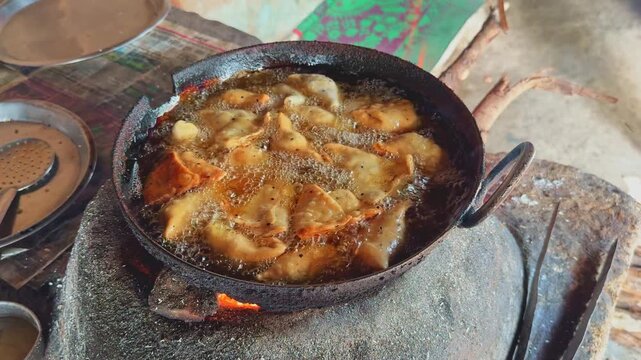 Golden samosas frying in bubbling oil on a traditional clay stove, creating a rustic Indian street food scene with rich aroma and sizzling texture.