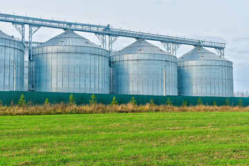 Modern metal silos with overhead conveyor, surrounded by verdant landscape