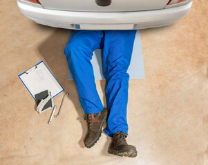 Top view of a mechanic on his back and working on the undercarriage of car with copyspace