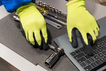 High-angle shot of an unrecognizable repairman's hands grabbing a tool from his toolbox and consulting his laptop for information about the car.