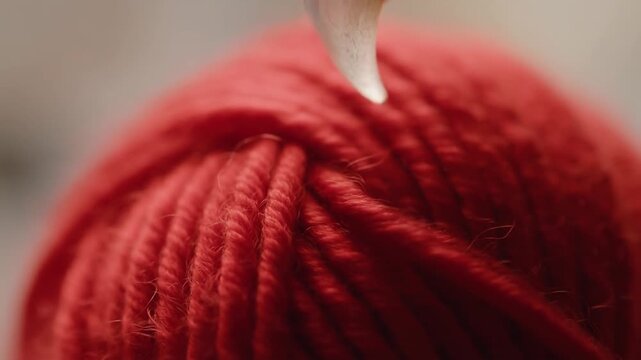 Macro shot of a red yarn ball, a sharp transparent cat claw delicately touching the thread against a blurred background, conveying a contrast of softness and sharpness.