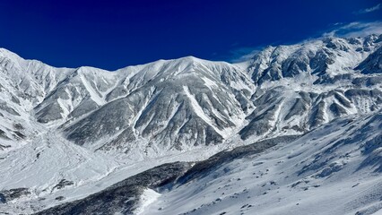 Fototapeta premium Steep Slope and Snowy Mountains under Bright Sky