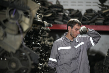 White man technician checking used car damaged engine block at scrap yard warehouse recycle area part. Maintenance engineer inspecting rust oily auto motor old spare part in junkyard for reuse service