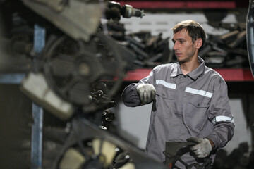 White man technician checking used car damaged engine block at scrap yard warehouse recycle area part. Maintenance engineer inspecting rust oily auto motor old spare part in junkyard for reuse service