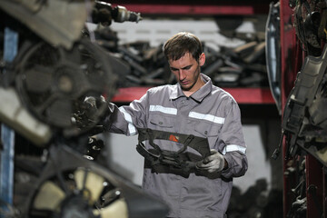 White man technician checking used car damaged engine block at scrap yard warehouse recycle area part. Maintenance engineer inspecting rust oily auto motor old spare part in junkyard for reuse service