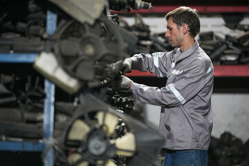 White man technician checking used car damaged engine block at scrap yard warehouse recycle area part. Maintenance engineer inspecting rust oily auto motor old spare part in junkyard for reuse service