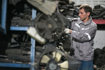 White man technician checking used car damaged engine block at scrap yard warehouse recycle area part. Maintenance engineer inspecting rust oily auto motor old spare part in junkyard for reuse service