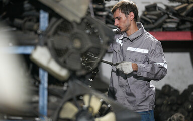 White man technician checking used car damaged engine block at scrap yard warehouse recycle area part. Maintenance engineer inspecting rust oily auto motor old spare part in junkyard for reuse service
