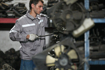 White man technician checking used car damaged engine block at scrap yard warehouse recycle area part. Maintenance engineer inspecting rust oily auto motor old spare part in junkyard for reuse service