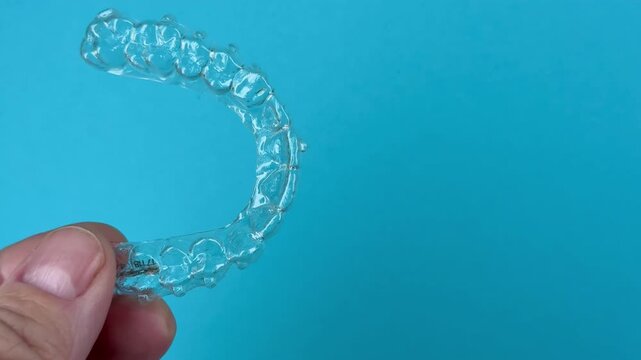 The doctor holds in his hand transparent aligners plastic braces retainers for straightening teeth on a blue background