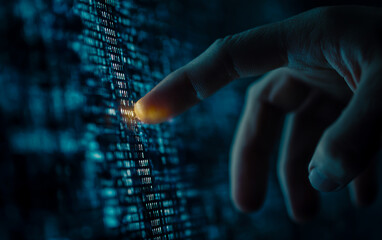Close up of a human finger touching a glowing digital screen with lines of code or data
