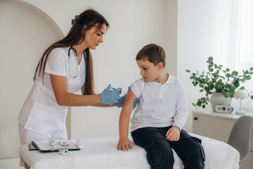 Fototapeta premium Gives an injection. Boy is in routine appointment in clinic with female doctor