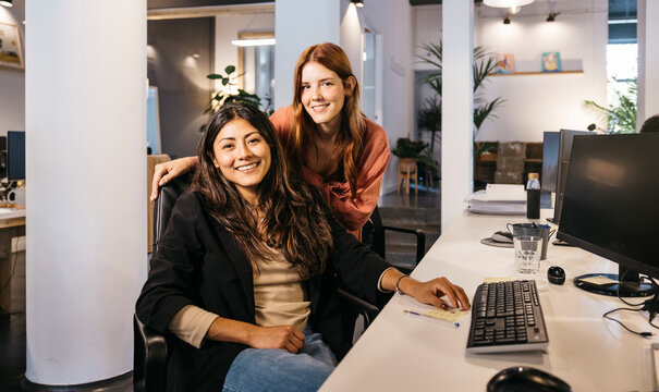 Two smiling women colleagues posing in an open-plan workspace