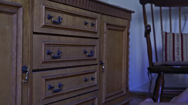 Someone's hand opens and closes a wooden drawer in an antique cabinet, neatly organizing personal belongings. An old chair is visible in the background, adding to the vintage home interior.