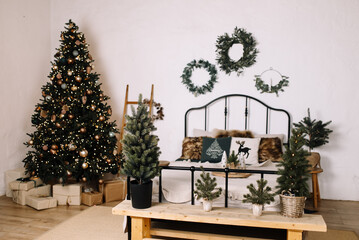 Cozy Christmas interior with a decorated Christmas tree, stylish decorative wreaths on the wall, and a bed with fluffy pillows.