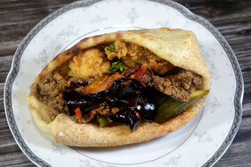 Mix of Fried beef brain, beef liver slices deep fried in oil and served with parsley in a traditional Egyptian flat bread with green pepper, pickled eggplant and cucumber
