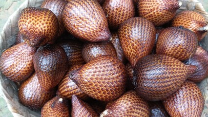 Fresh salak fruits in a basket, showing shiny brown scaly skin texture.