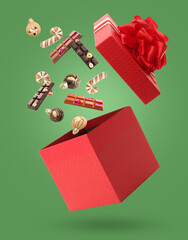Christmas celebration. Chocolate candies and cookies falling into gift box on green background