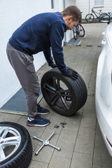 Young man changing the punctured tyre on his car loosening the nuts with a wheel spanner before jacking up the vehicle