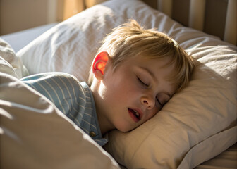 Blond boy sleeps peacefully on soft pillow in his bed. Sunlight gently illuminates his face. He rests comfortably, eyes closed, mouth slightly open in deep slumber.