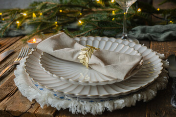 Christmas dinner table setting. White plates decorated napkin and golden ring on rustic wooden table. 