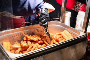 preparing fried sweet churros street food in the city center at the Christmas market in Krakow, Poland.